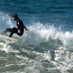 Male surfer in black wetsuit and hood making a turn