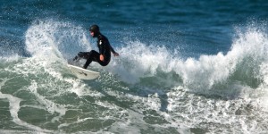 Male surfer in black wetsuit and hood making a turn